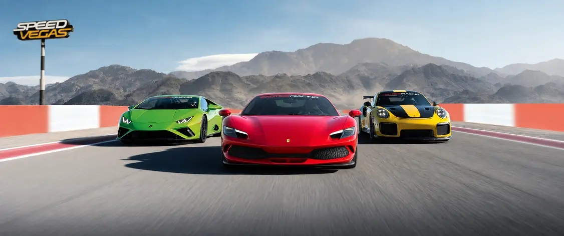 Three colorful sports cars—a red, a green, and a yellow—race on a track against a mountainous backdrop under a clear blue sky. The scene exudes excitement and speed.